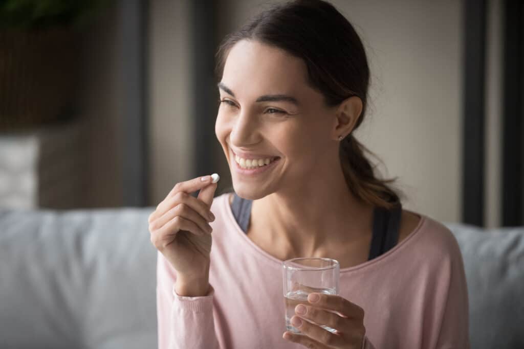 Nice young woman smiling, taking a pill